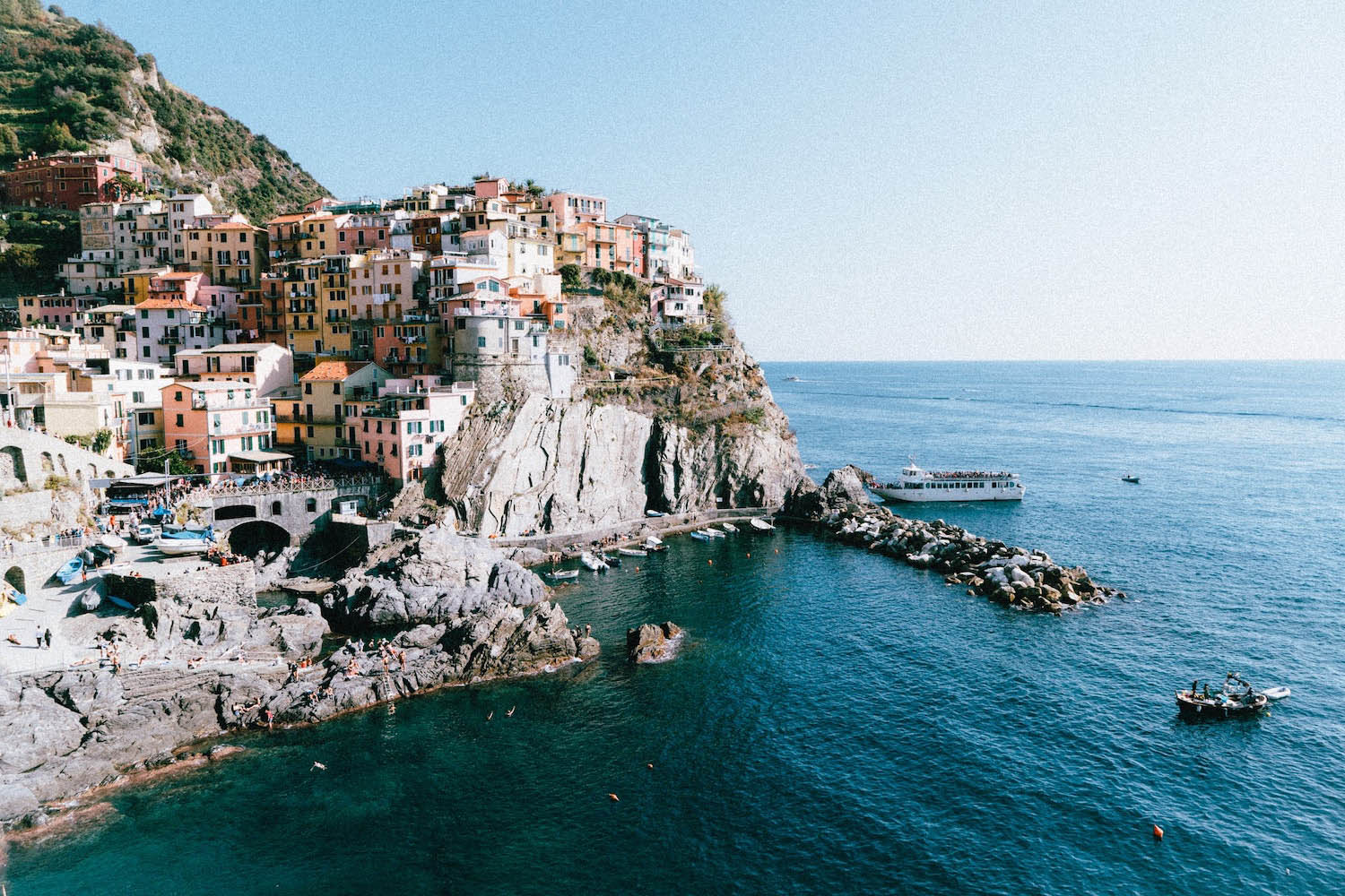 Colorful Houses of the village of Manarola, Italy, with natural rocks, the clear blue water and a boat in the background
