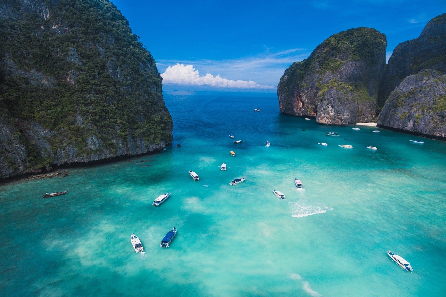Drone shot of Maya Bay in Phi Phi Island, Krabi, Thailand with many boats sailing on clear blue water and natural rocks