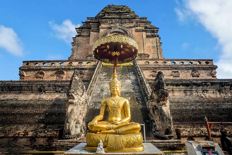 Wat Chedi Luang temple in Chiang Mai with a golden Buddha image and a ruined temple on a sunny day