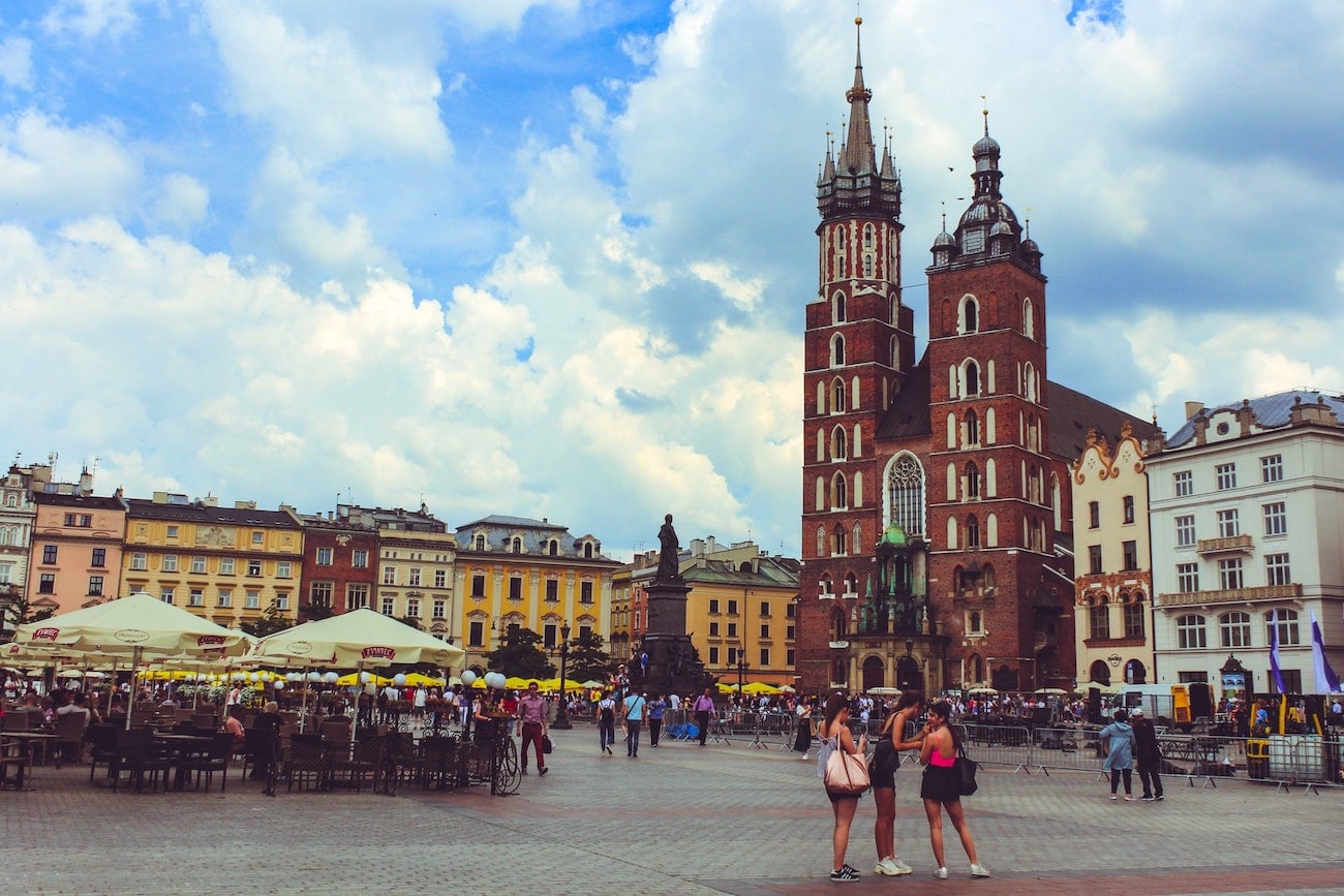 Main square of Krakow, Poland, with red brick buildings, tourists taking photos, and restaurants serving customers