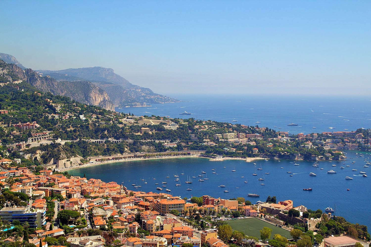 Bay of Nice, France with red roof houses, a sandy beach, and clear blue water with lots of boats