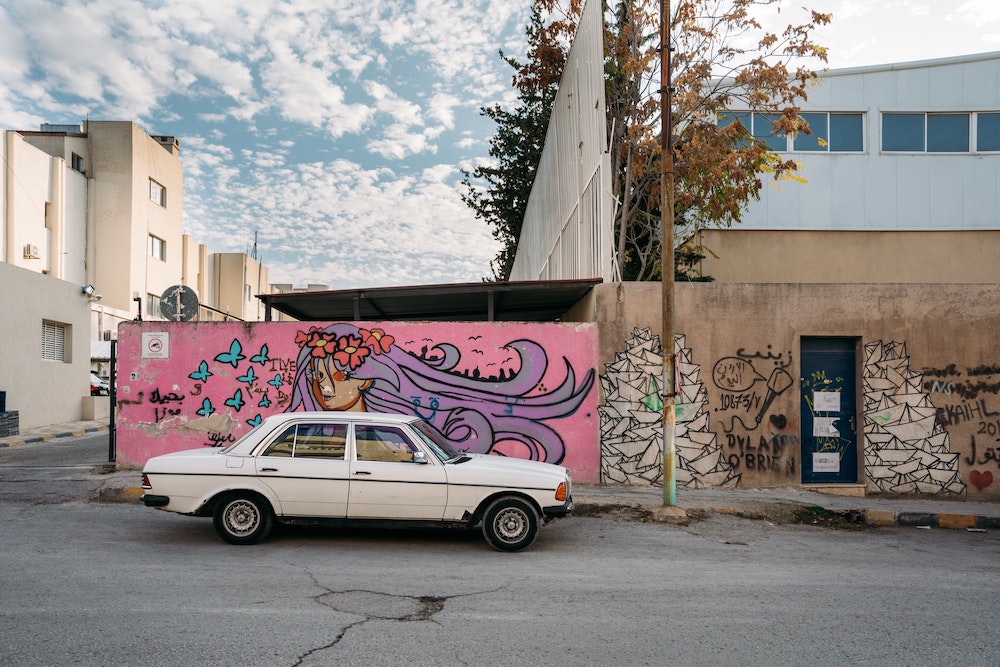 a white car in Amman with street art in the background