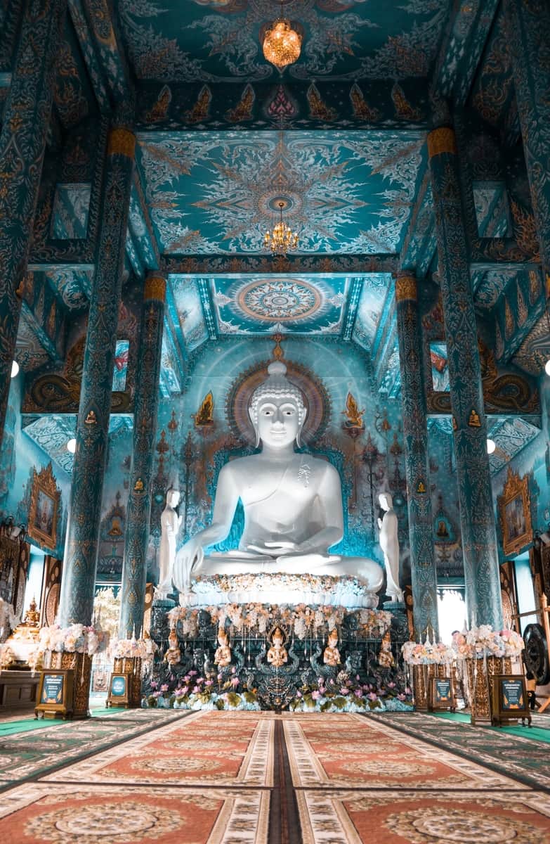 Inside the blue Temple in Chiang Rai with a white Buddha and carpeted floor
Thailand-itinerary-Visit-Chiang-Rai in Northern Thailand