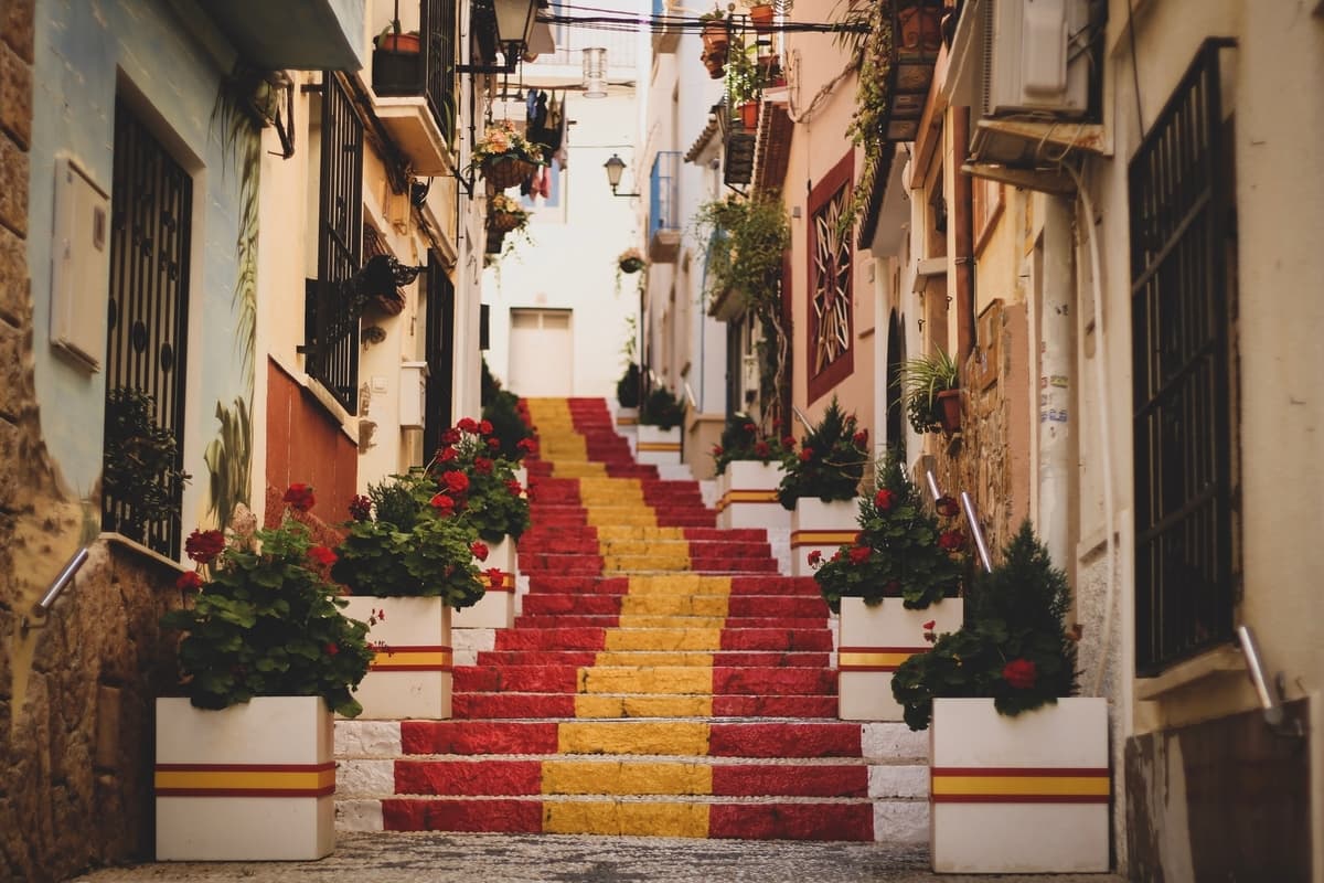 Alley with stairs displaying the colors of Spain and hanging plants.