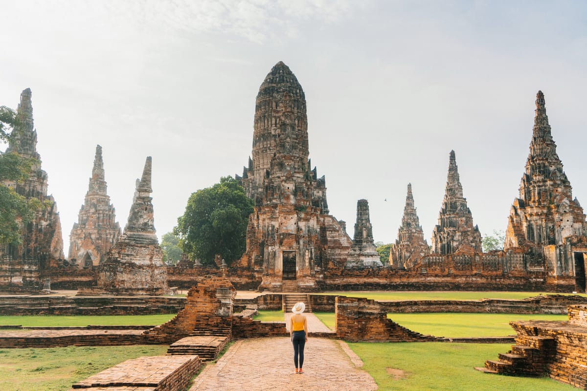 Temple ruins on a sunny day with a woman standing in front of the complex. Ayutthaya Tour from Bangkok