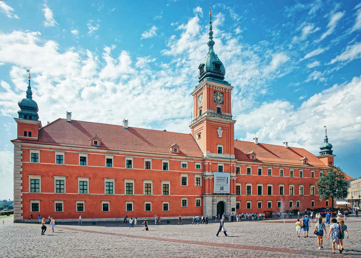 Enter the Royal Castle in Warsaw - A historic red-brick castle complex with a tower under a sunny sky.