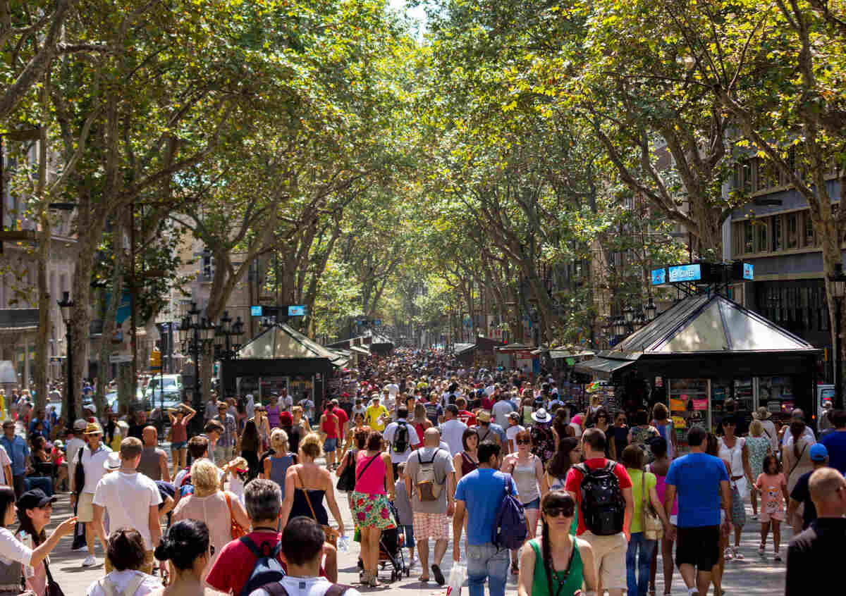 Photo of a busy street in Barcelona with many visitors and trees on a sunny summer day