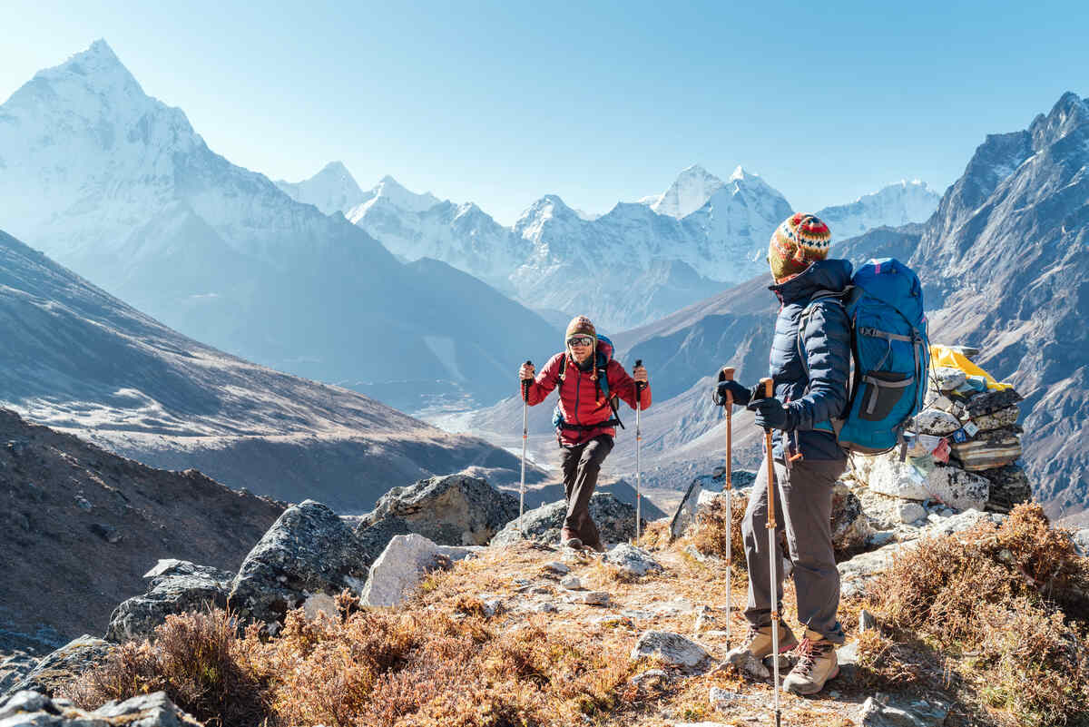 Couple following Everest Base Camp trekking route near Dughla 4620m. Backpackers carrying Backpacks and using trekking poles and enjoying valley view in Nepal