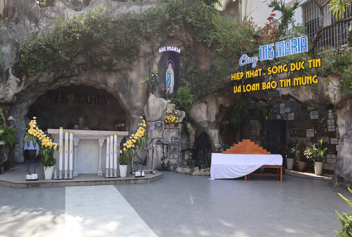 Cave entrance with a religious altar and visitors. Da Nang Cathedral behind with the grotto
