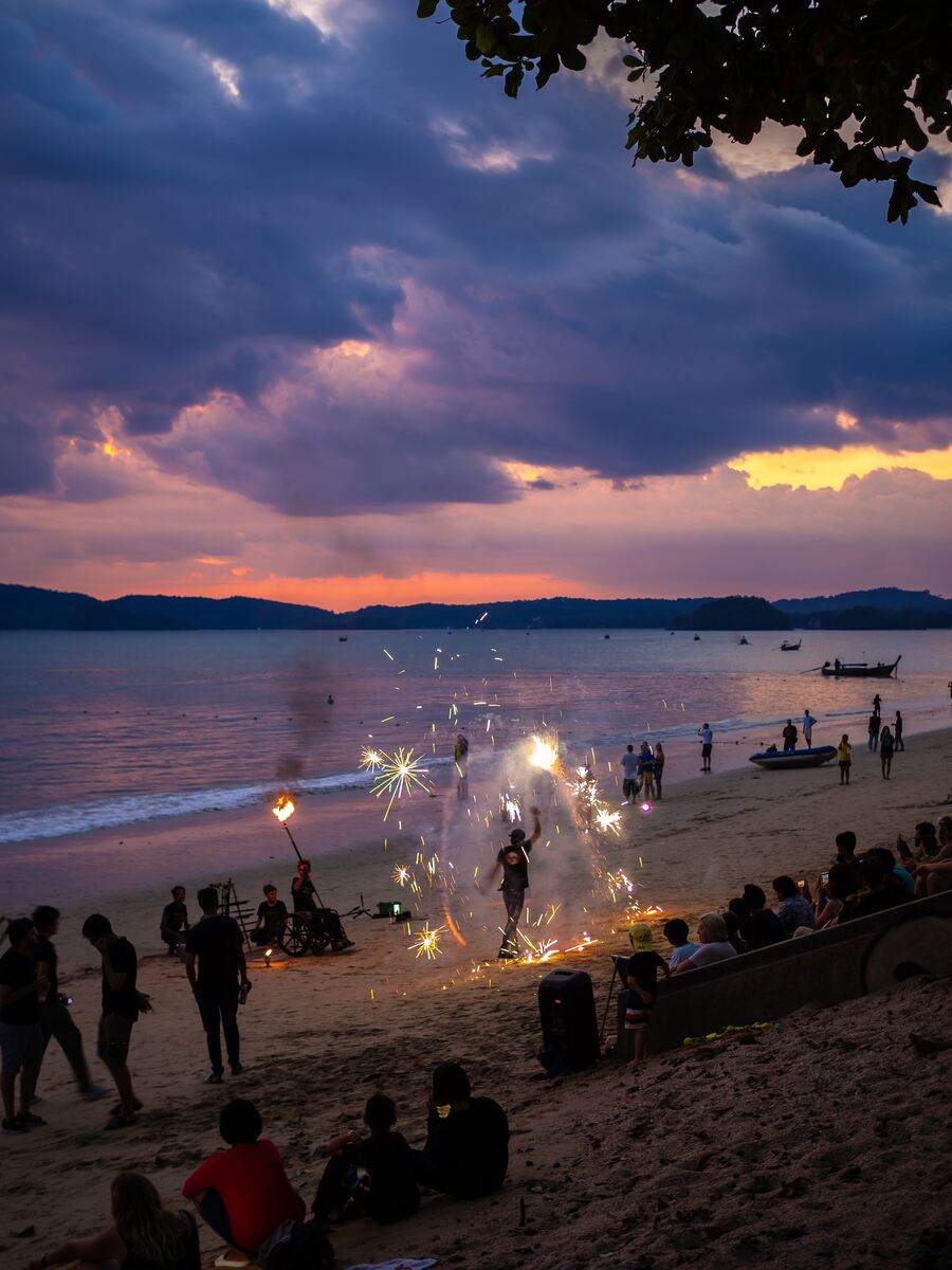 Crowded beach with sunset and bonfires.