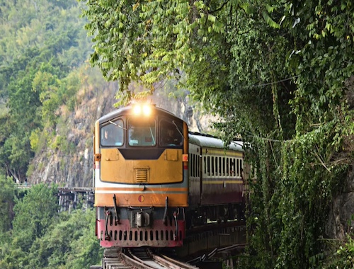 A rustic train moving on tracks through a lush green forest, with sunlight streaming through the trees.