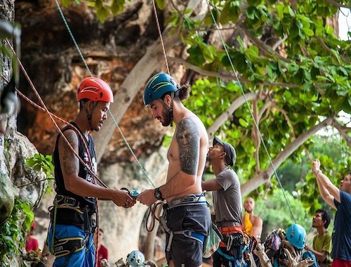 Two men rock climbing, exchanging gear.