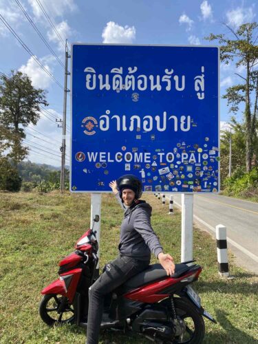"Welcome to Pai" sign in Thai and English and a tourist on a motorbike.