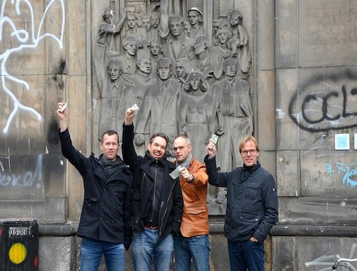 Four men posing happily in front of a historic relief.