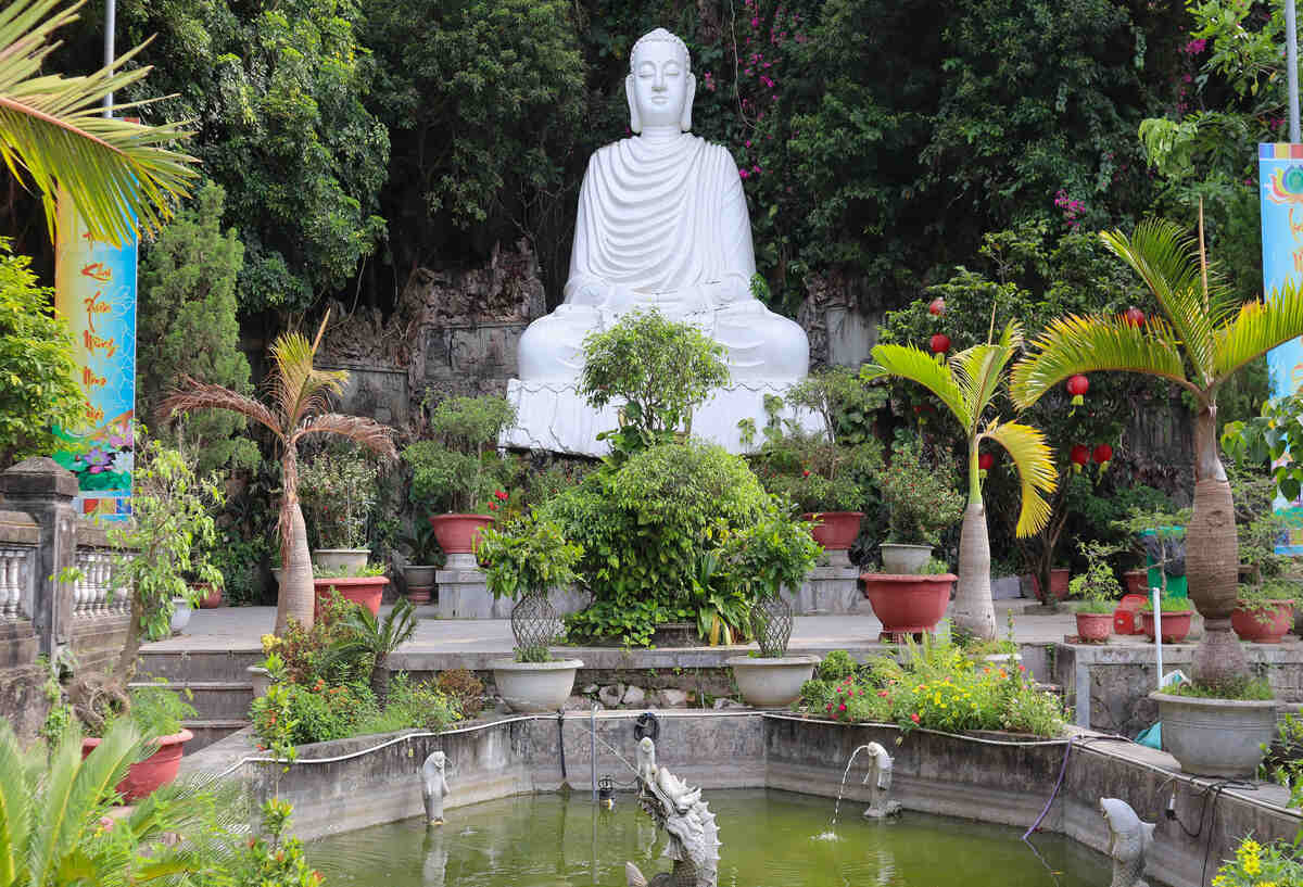 Tall white Buddha statue in a garden setting.