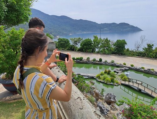 Woman taking a photo of a landscaped pond with a view of the ocean.