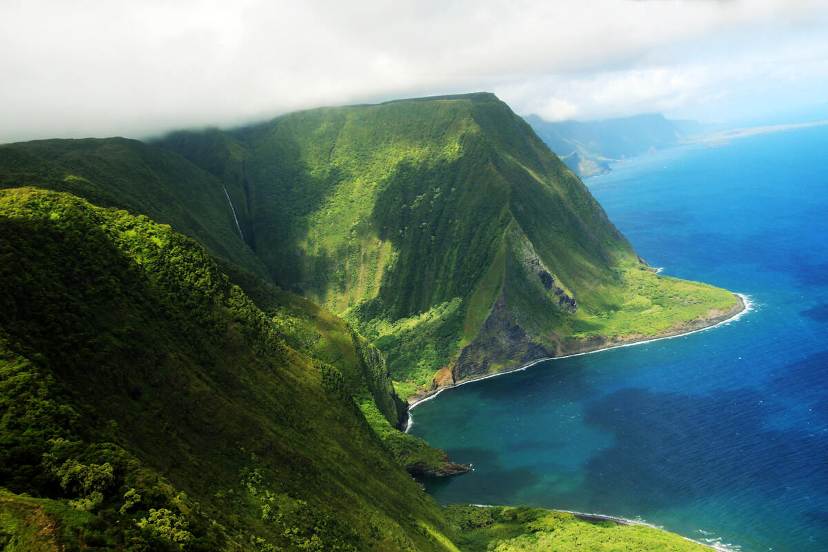 Aerial view of a steep, green mountain and coastline. Moloka‘i-Island-Is-This-The-Hidden-Gem-of-Hawaii