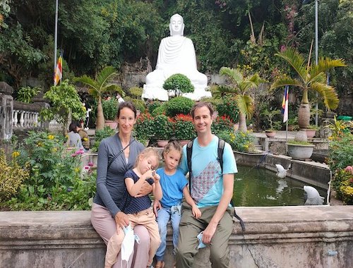 Family posing in front of a temple with Buddha statues.