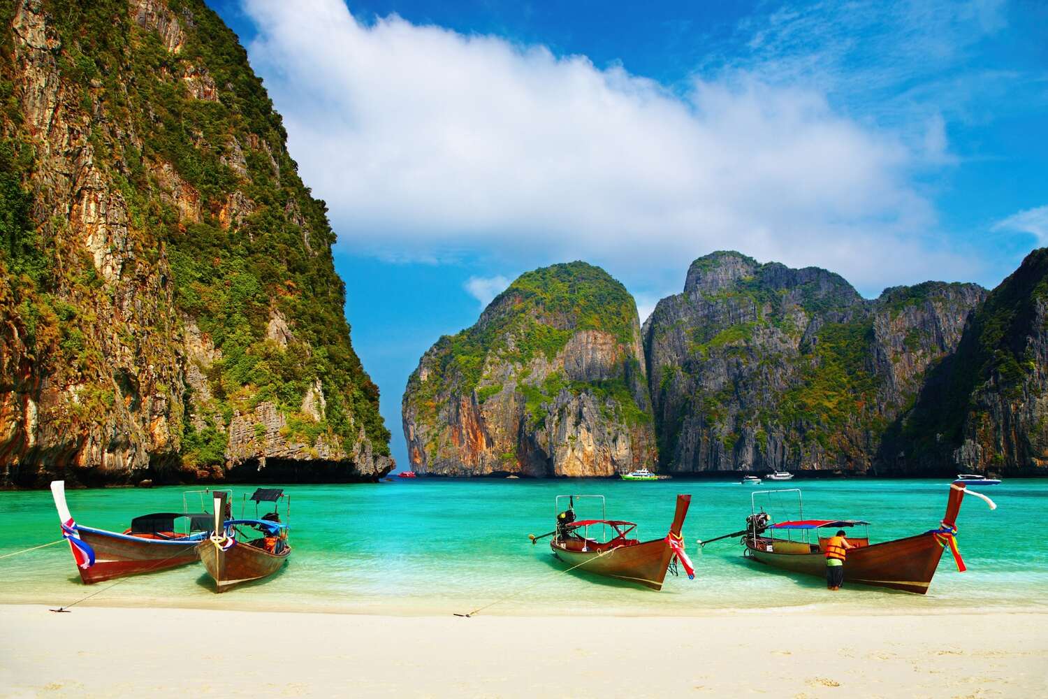 Boats on clear water with limestone cliffs in Thailand in May