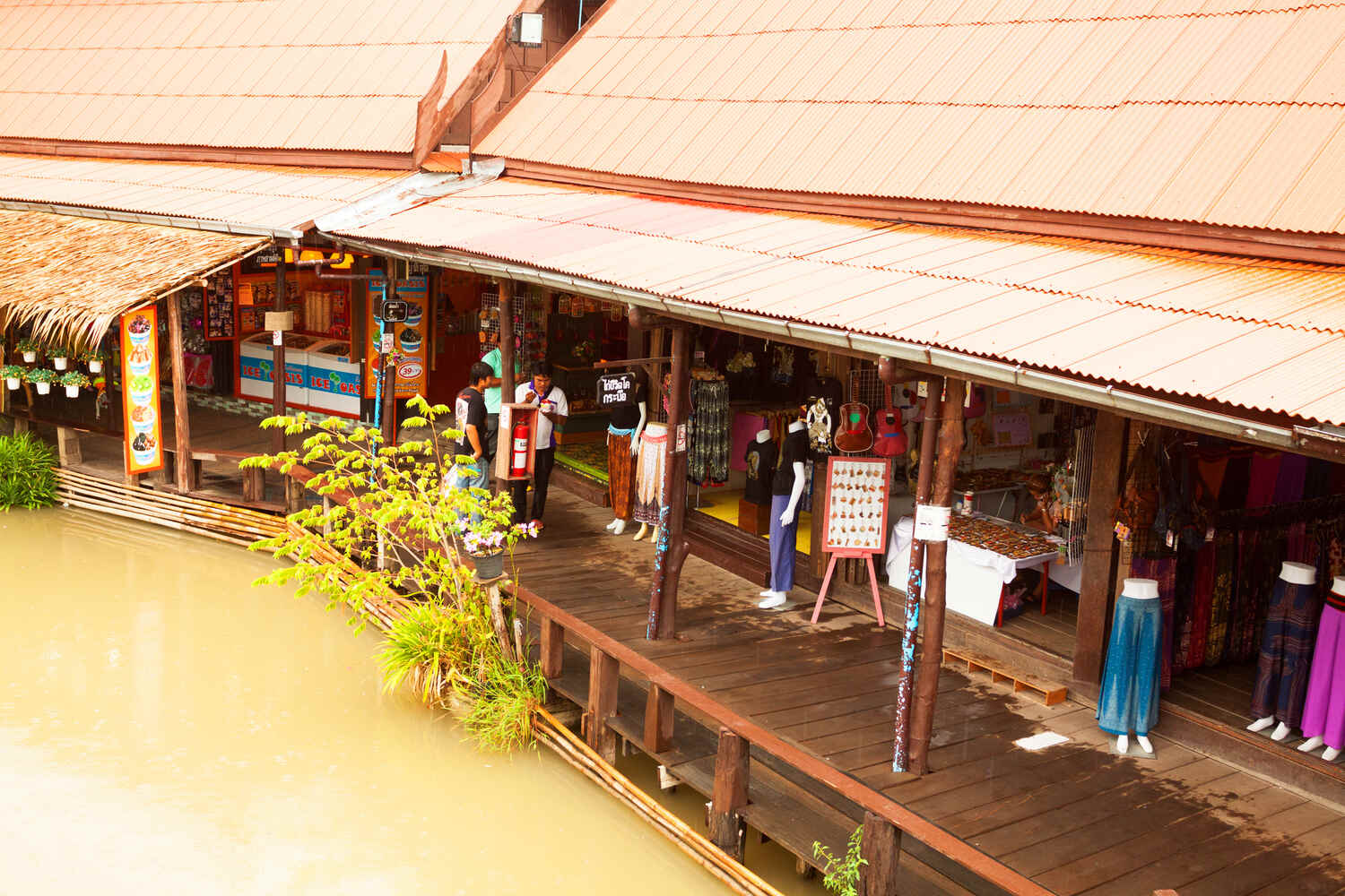 A traditional Thai market on stilts over water, with shops displaying clothing and souvenirs.