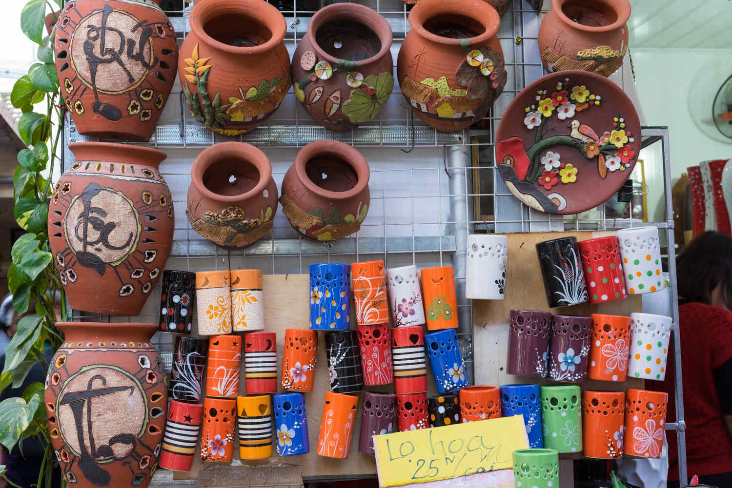 Colorfully painted ceramic pots and plates displayed on a wall in a vibrant outdoor market.