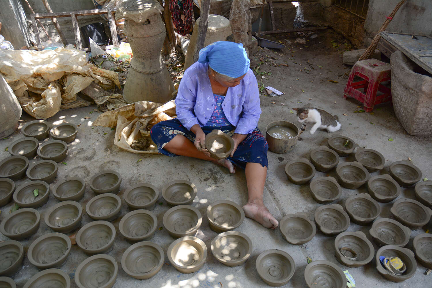 Traditional Vietnamese pottery making with an elder woman crafting bowls in an outdoor workshop.