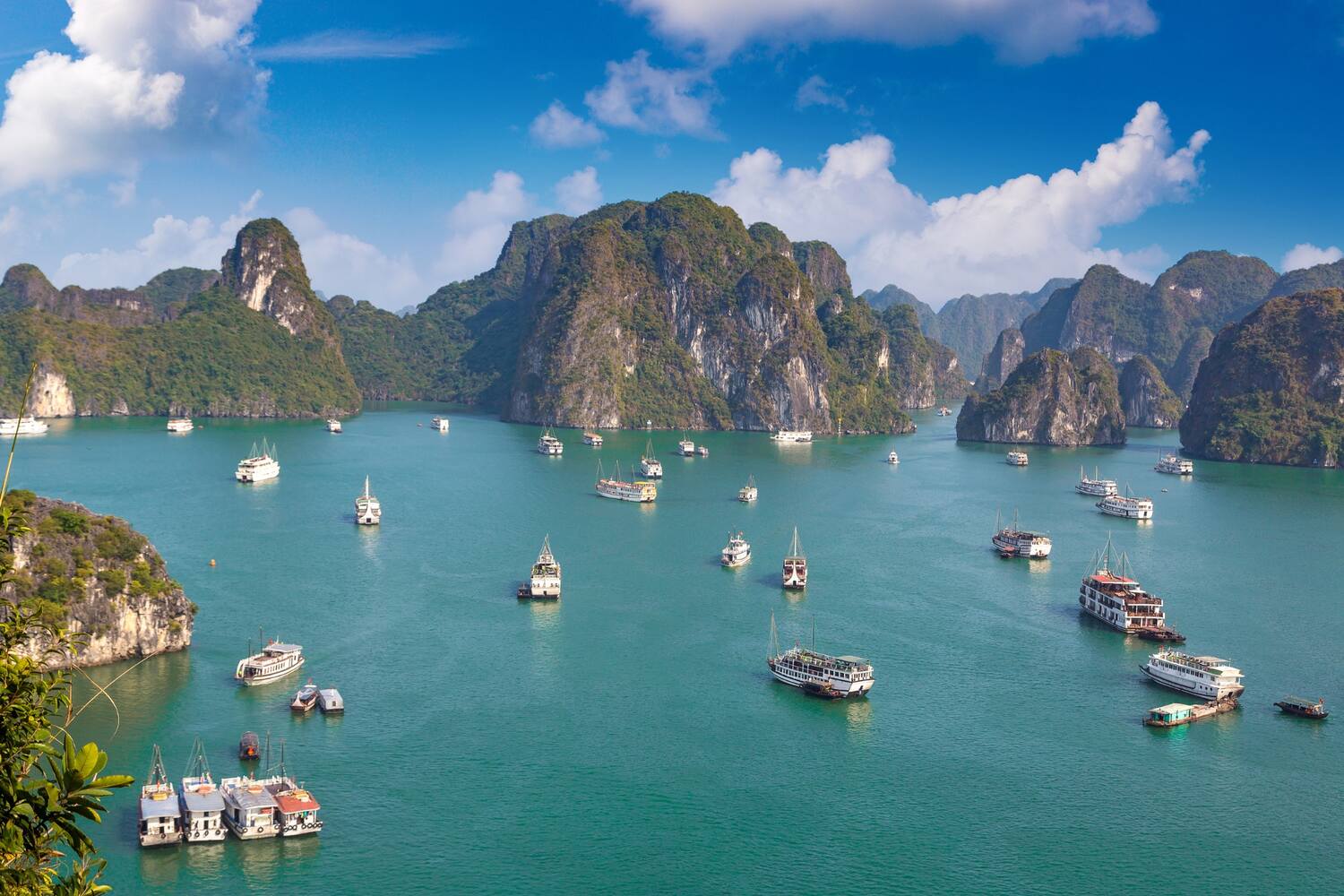Dramatic limestone cliffs rising from emerald waters with boats anchored below.
