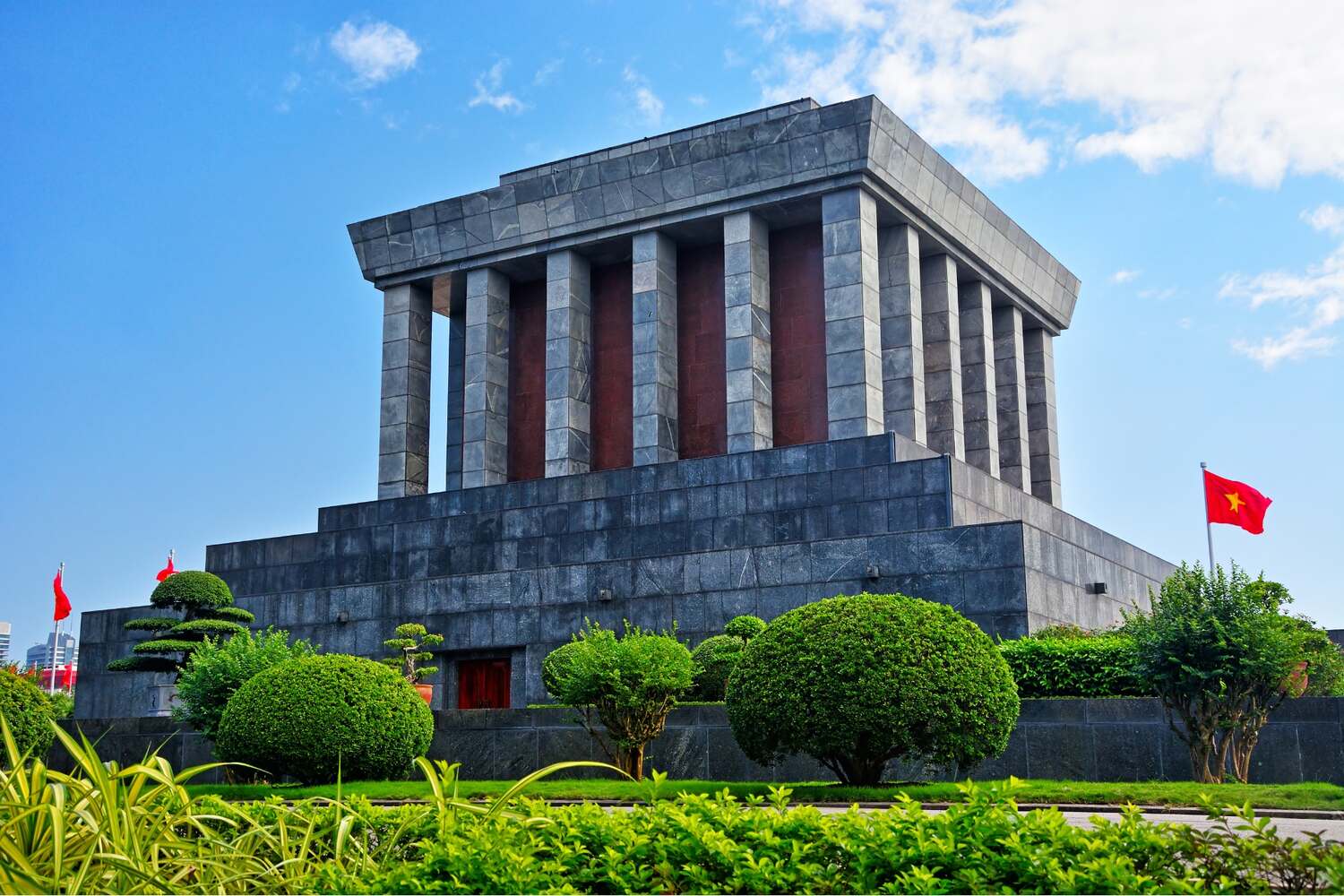 Ho Chi Minh Mausoleum in Hanoi, an imposing gray building with Vietnamese flags and manicured greenery.