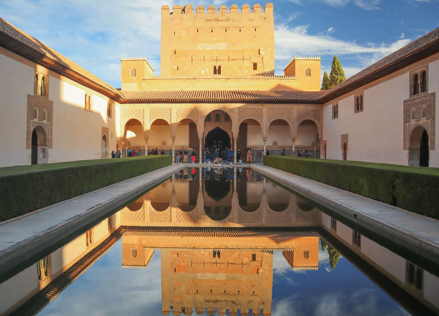 The Alhambra's Court of the Myrtles with its reflective pool under a clear sky in Granada, Spain.