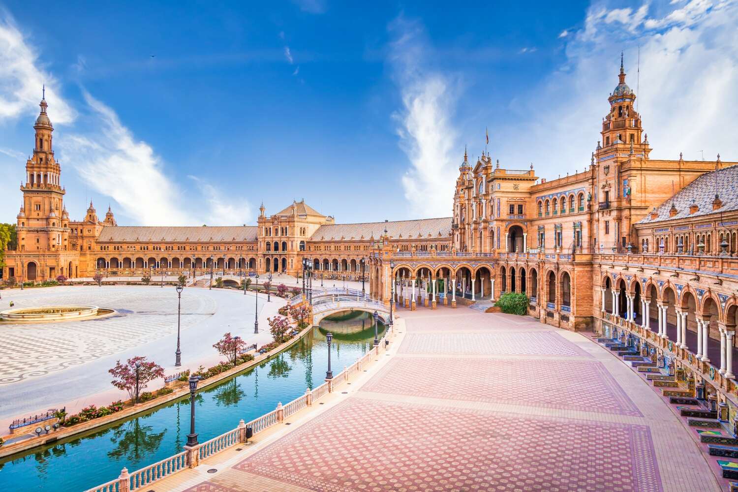 Seville's Plaza de España with its semicircular brick pavilion and water canal under a clear sky.