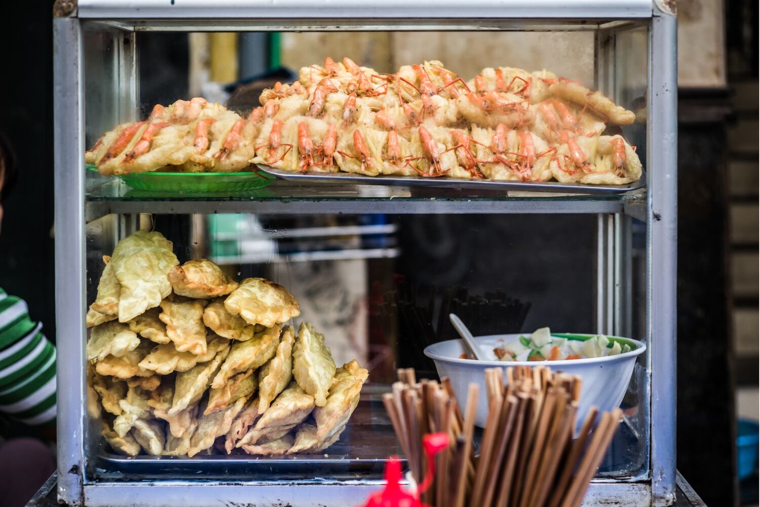 Street food stall in Vietnam showcasing a glass case filled with crispy fried spring rolls.