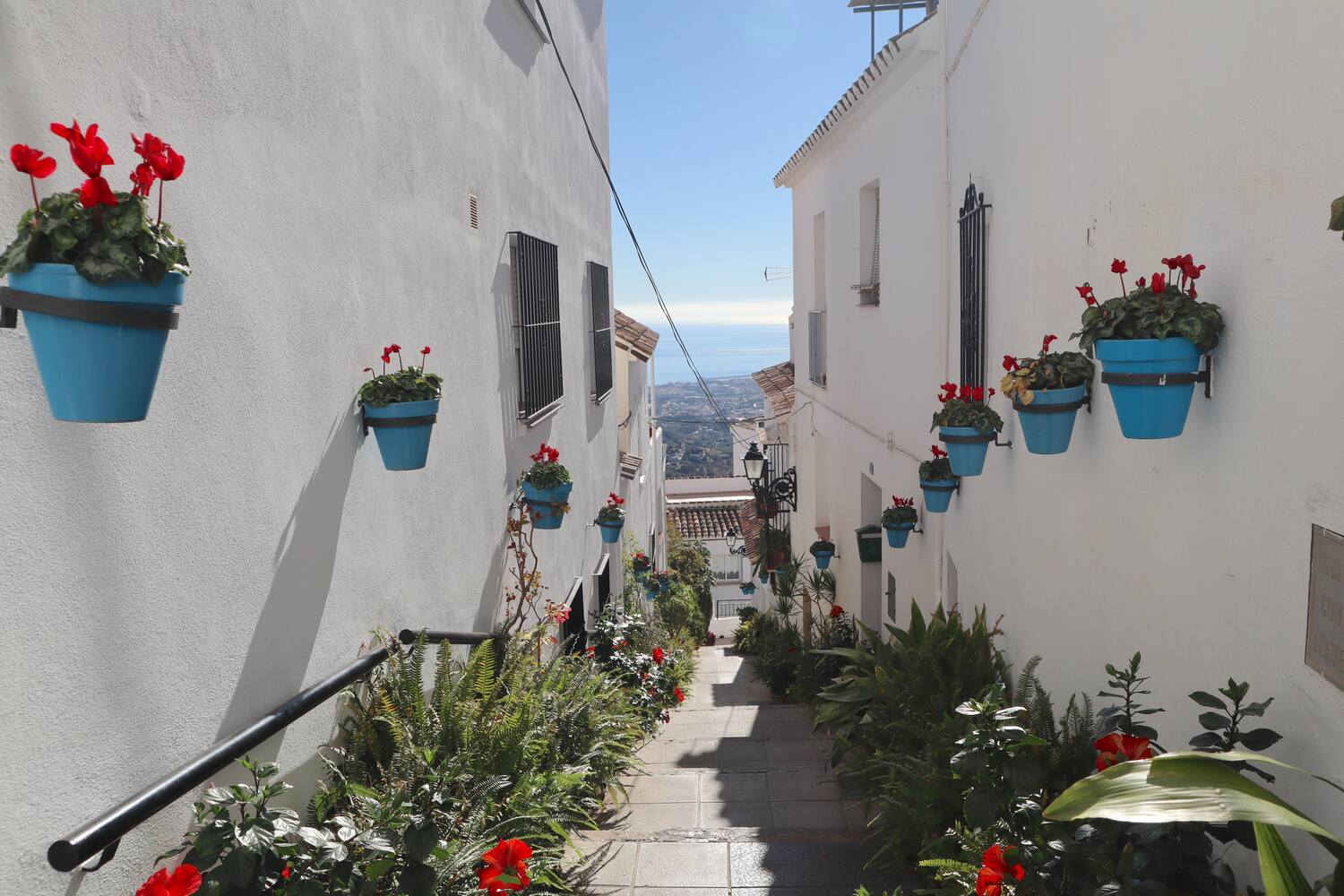 White-washed Andalusian village with hillside homes and blue ocean in the distance.