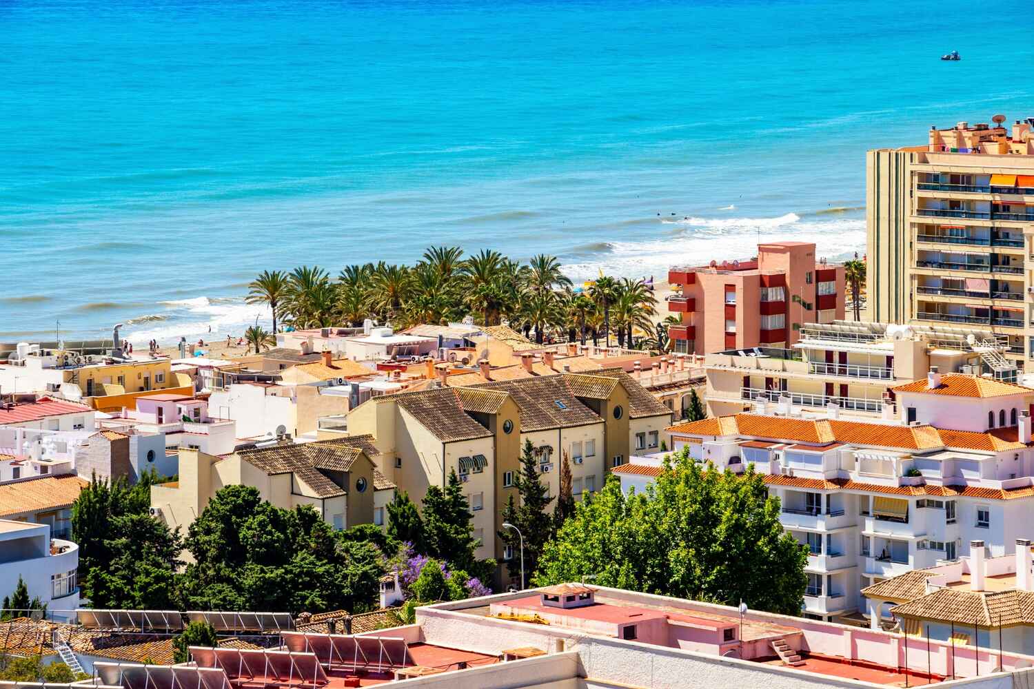 Sandy beachfront lined with buildings in Torremolinos, Spain, and turquoise Mediterranean waters.