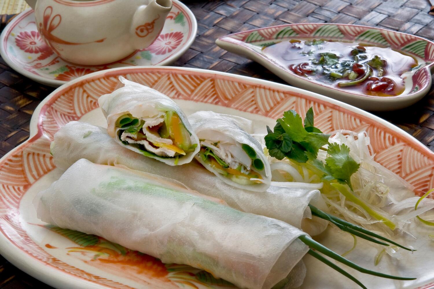 Fresh spring rolls beside dipping sauce on a plate garnished with herbs.