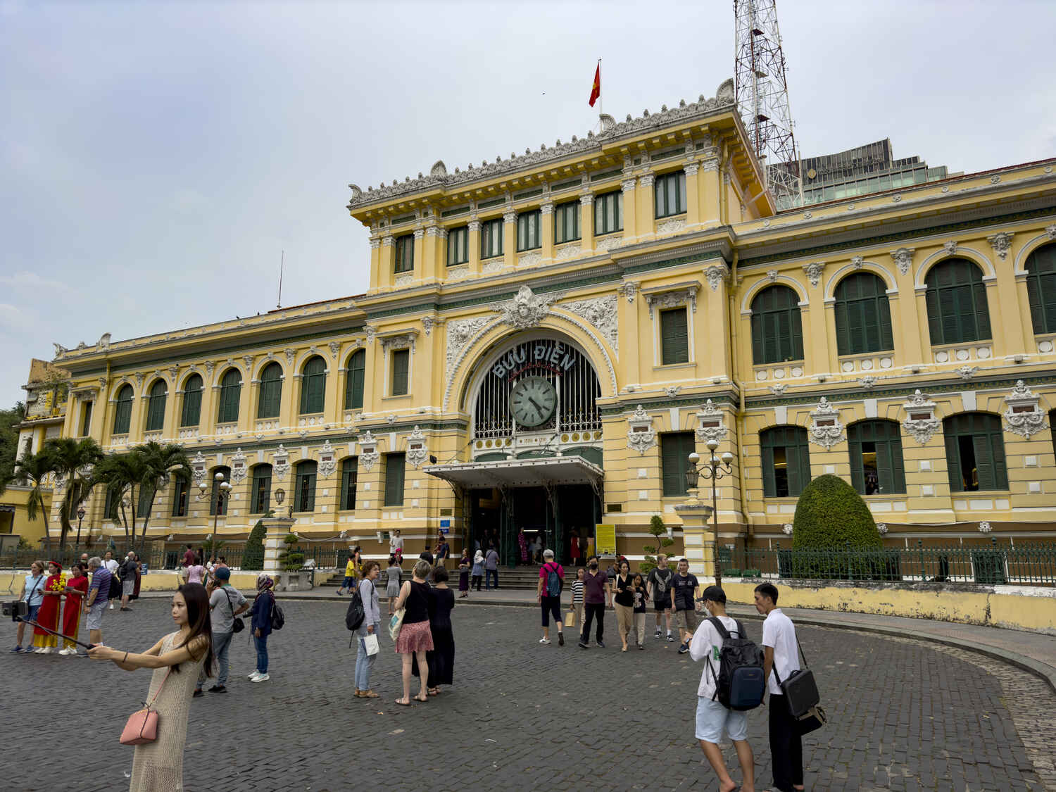 Frontal view of the colonial-era Central Post Office in Ho Chi Minh City with visitors milling about the entrance.