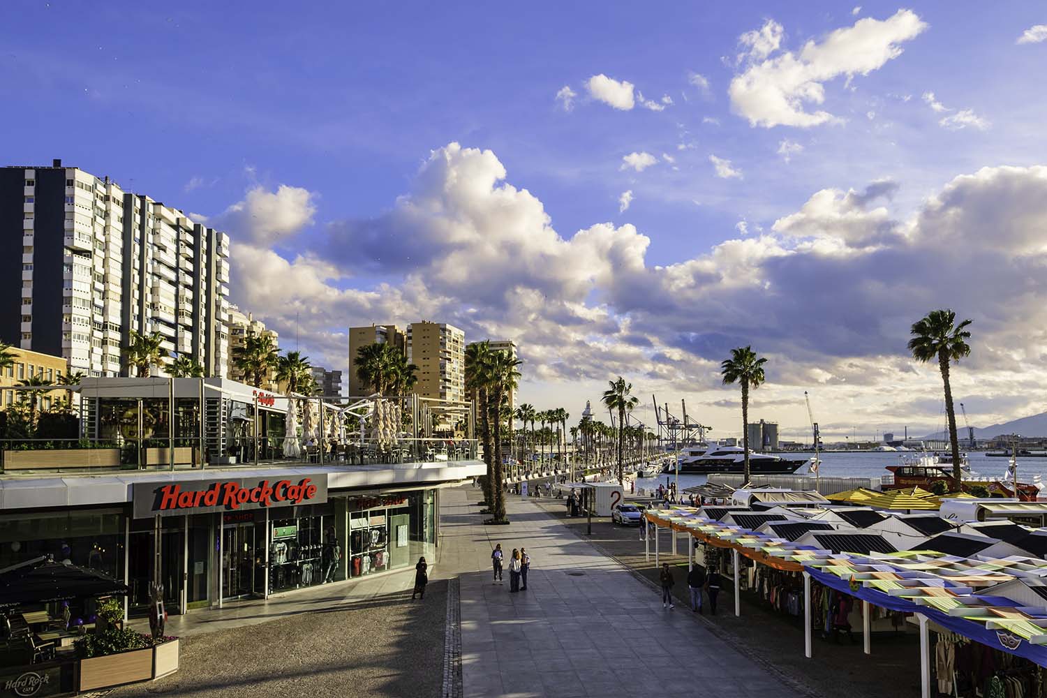 People strolling at the Muelle Uno in Malaga, the tourist harbor but also a commercial area and a place for meeting. Among the numerous cafes and restaurants, people can relax at the Hard Rock Café, with food and music.