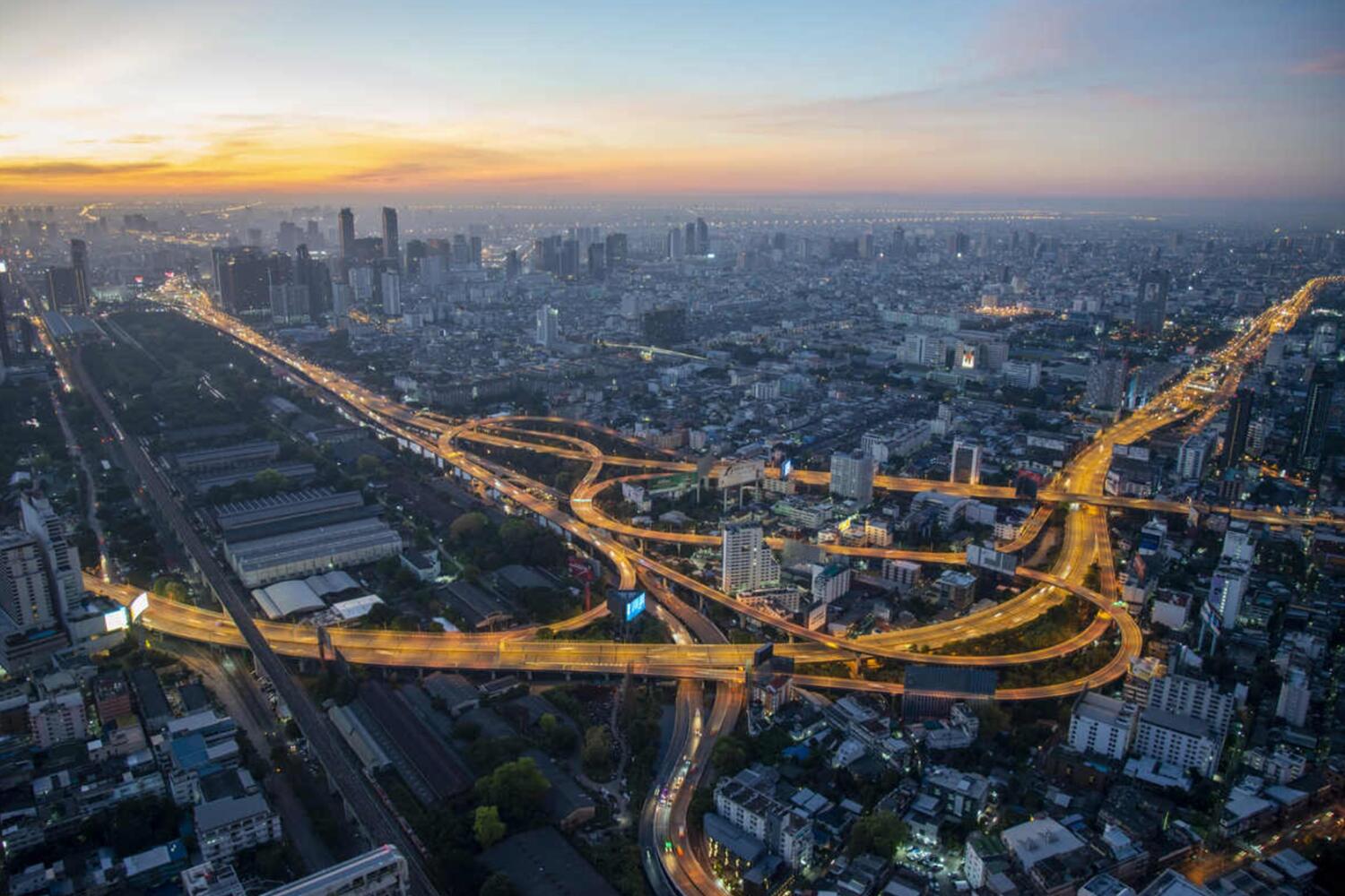 Aerial view of Bangkok at twilight with lit highway and buildings.